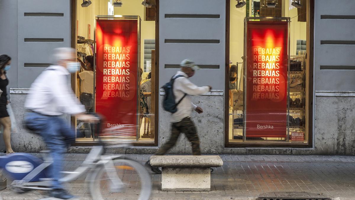 Archivo - Varias personas pasan al lado del escaparate de una tienda donde se observan carteles indicativos de rebajas en Valencia