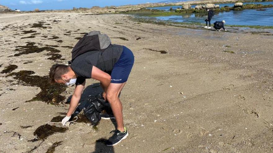 Un participante recoge un trozo de plástico semienterrado entre algas y arena. 