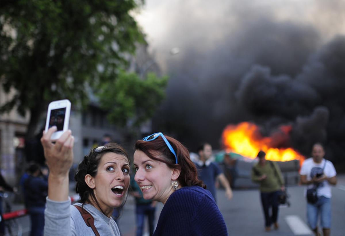 Unes turistes es fan un ’selfie’ amb uns contenidors cremant de fons aquest dijous, a Barcelona.