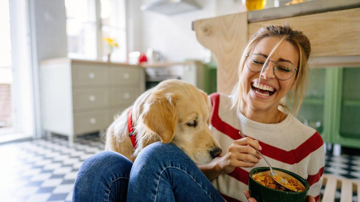 Chica comiendo y riéndose con un perro