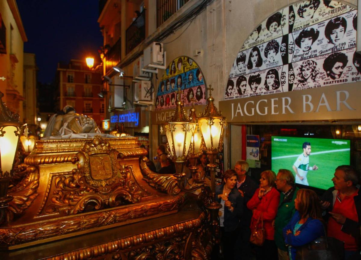 Un paso recorre las calles de Alicante, junto a un pub donde proyectan fútbol.