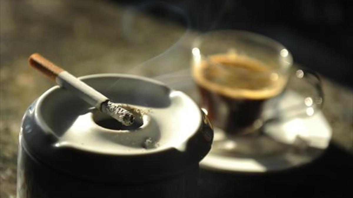 Un cigarrillo humea junto a una taza de café en un bar.