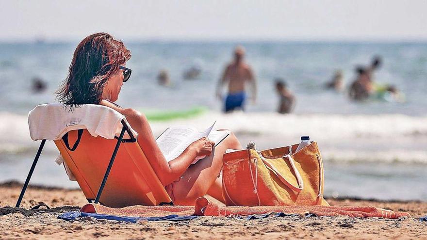 Una mujer lee sentada en una silla en una playa.