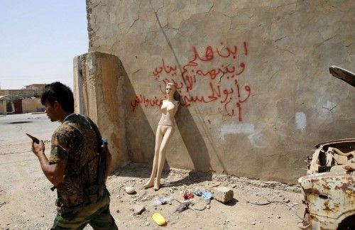 A Kurdish Peshmerga fighter walks past a mannequin leaning on the wall of the former headquarters of Islamic State militants in Sulaiman Pek