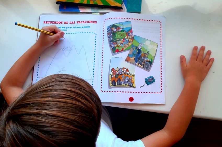 Un niño comenta los recuerdos de sus vacaciones en un cuaderno de verano