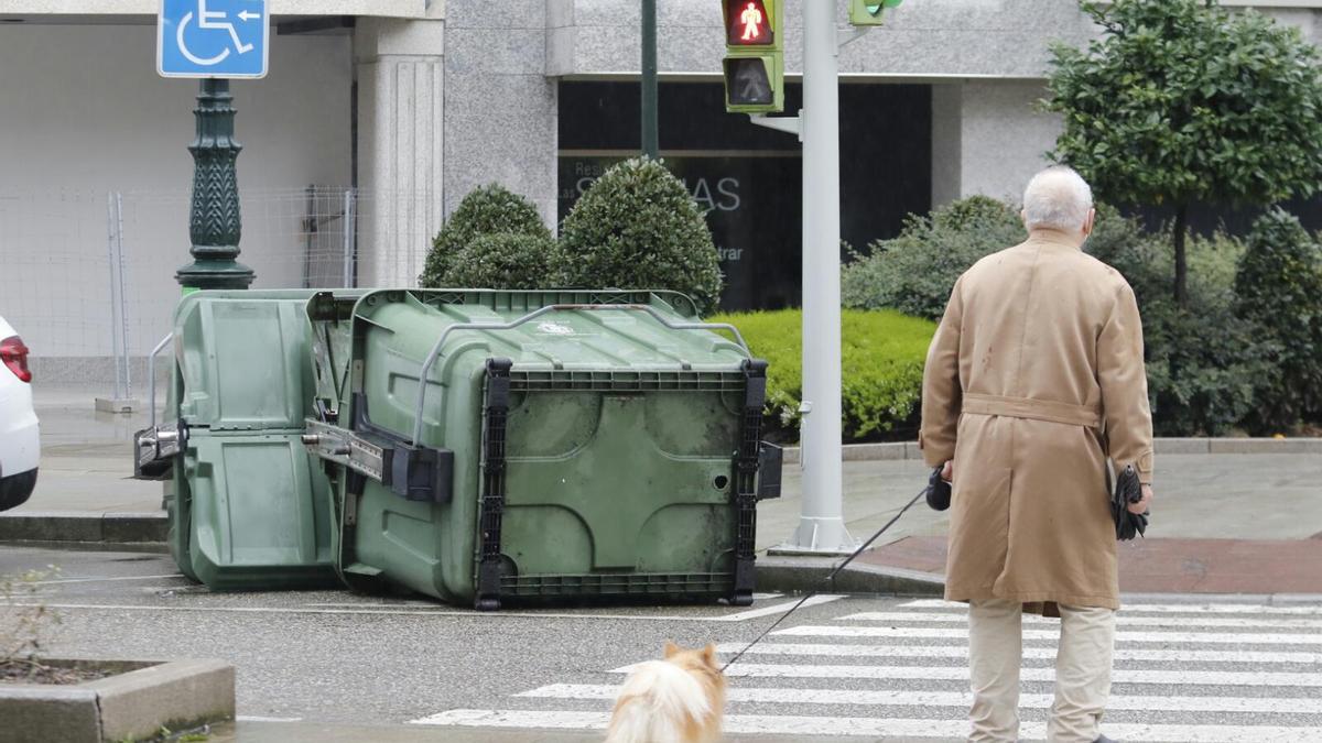 Un viandante pasea a su perro mientras observa contenedores caídos por la brutalidad de Karim