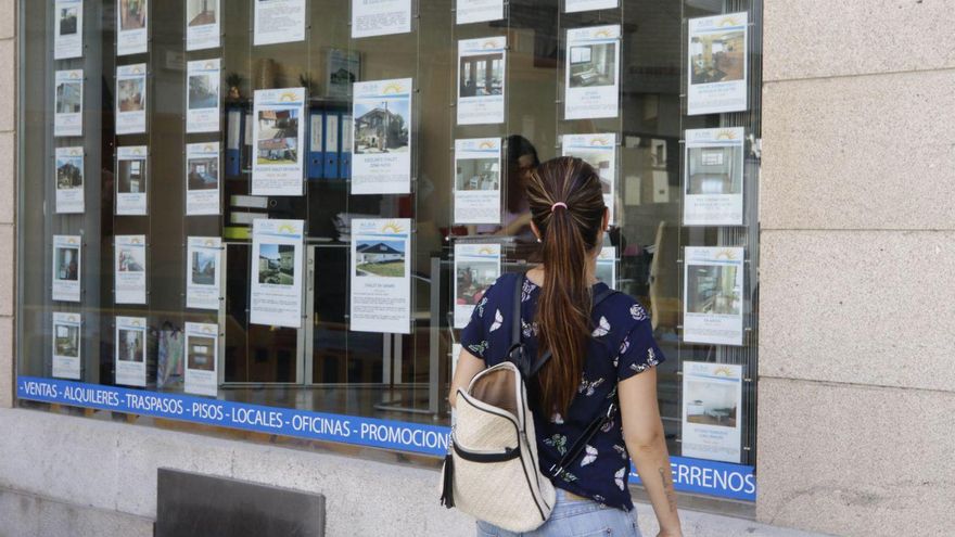Una joven viendo anuncios de pisos en el escaparate de una inmobiliaria de Vigo.