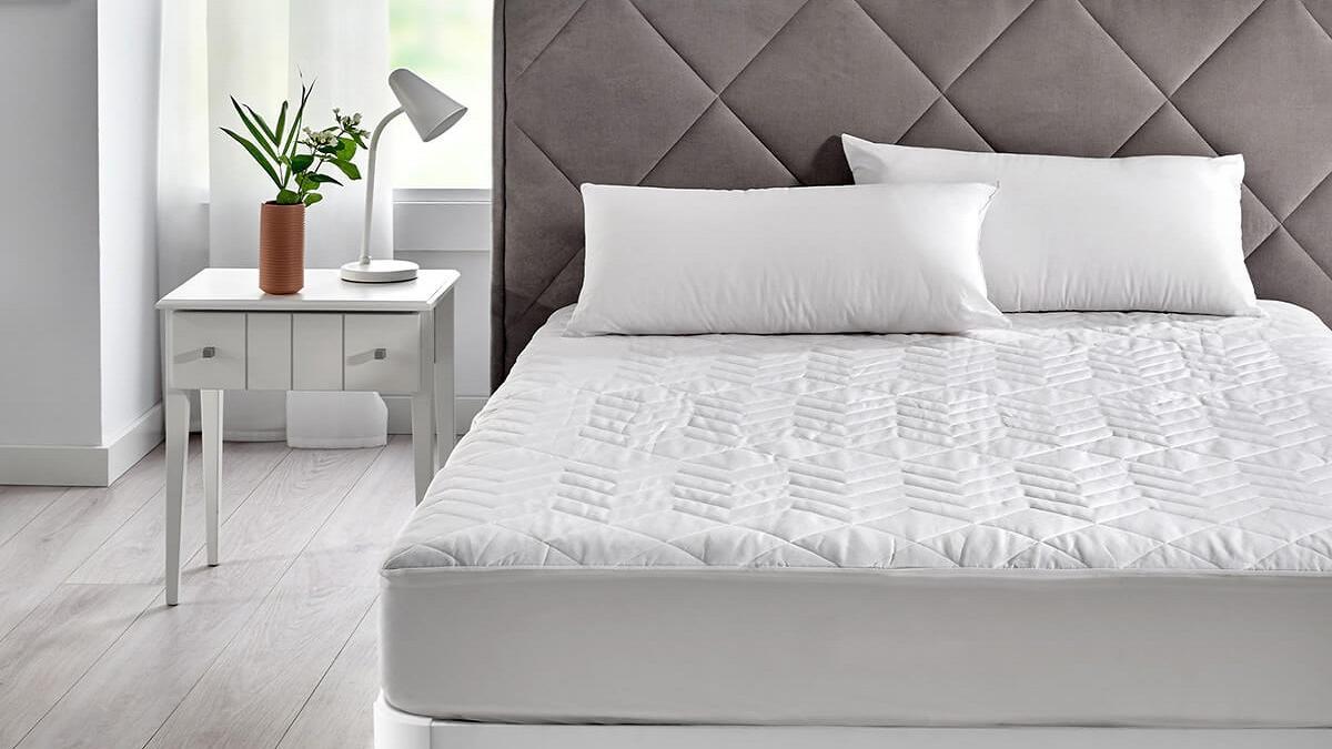 Una habitación en tonalidades blancas con una cama compuesta por somier y colchón.