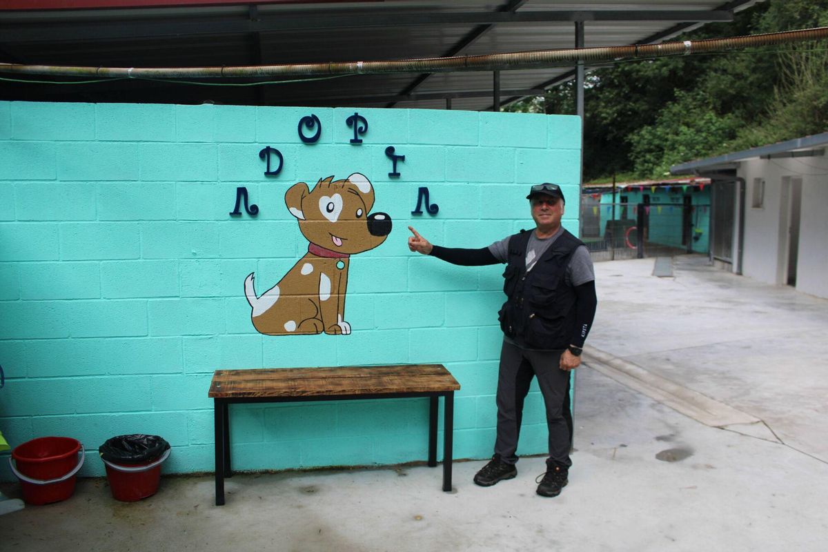 Reportaje perrera albergue de animales de Mieres trabajos de adecuación a cargo de Dog Hamony Paulino Fernández señalando adopta y el voluntario Arturo Suárez jugando con el perro Chuso