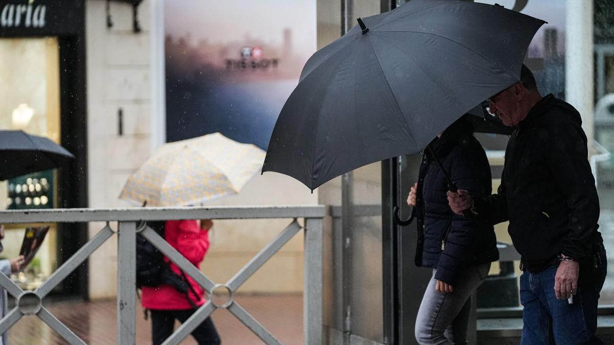 Sevillanos protegiéndose de la lluvia y el viento.