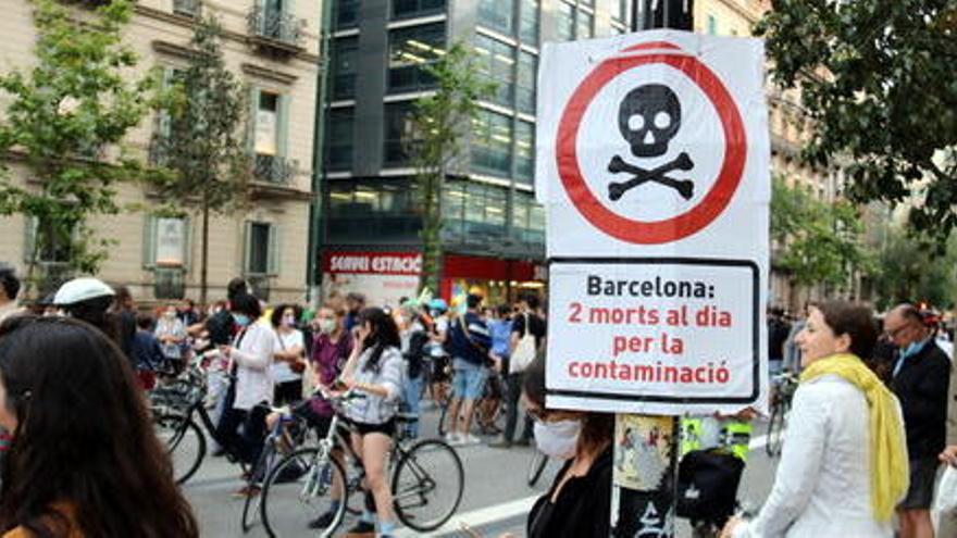 Un cartell que diu que la contaminació mata amb una manifestació contra els cotxes darrere, al centre de Barcelona