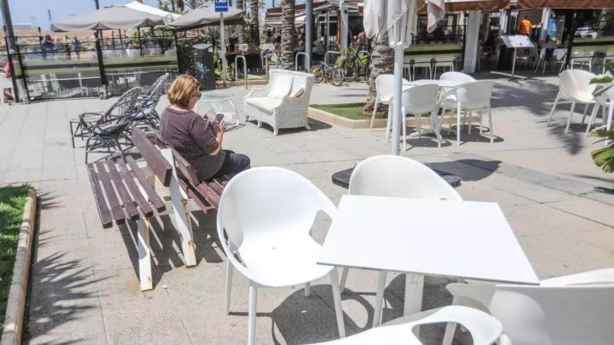 Banco del paseo rodeado por sillas y mesas de una de las terrazas que este lunes ha tenido que reducir su ocupación del paseo