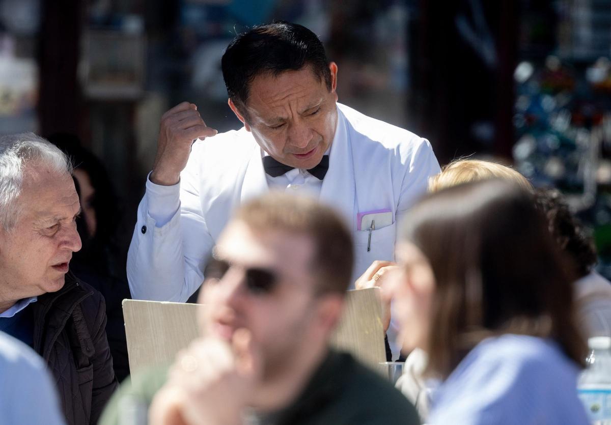 Un camarero de nacionalidad extranjera atiende una mesa en una terraza en el centro de Madrid.