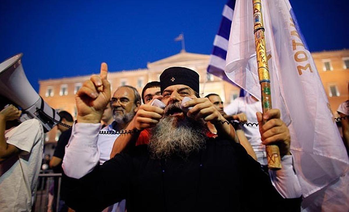 Un monjo ortodox grec parla als manifestants concentrats davant del Parlament a Atenes aquest dilluns en les protestes contra les mesures d’austeritat aprovades a la Cambra. El mateix dia, l’agència de qualificació Standard and Poor’s ha rebaixat la qualificació del deute grec.