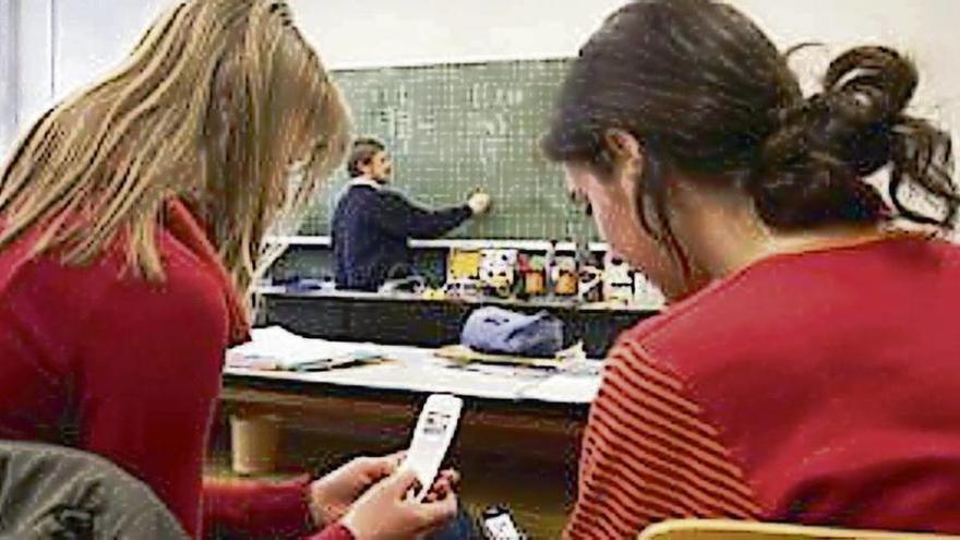 Dos alumnas consultan sus teléfonos móviles durante una clase.