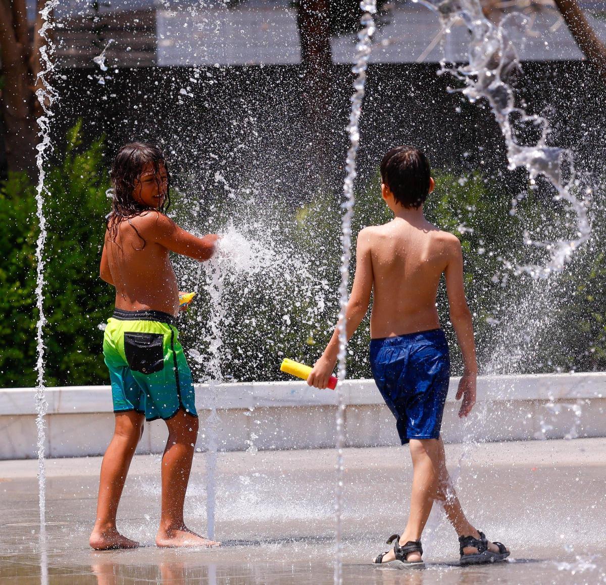 Niños disfritando del agua de una fuente en un espacio público.