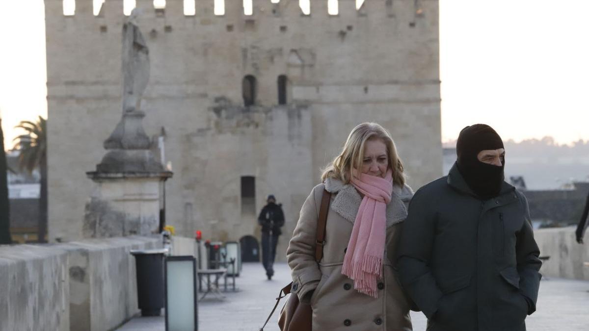 Una pareja se protege del frío mientras camina por el Puente Romano de Córdoba.
