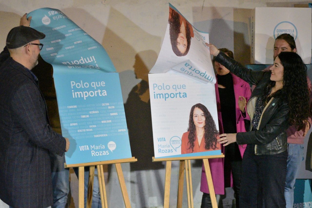 La candidata a la alcaldía de Santiago descubre el cartel electoral de Compostela Aberta junto al exalcalde de Santiago Mariño Noriega