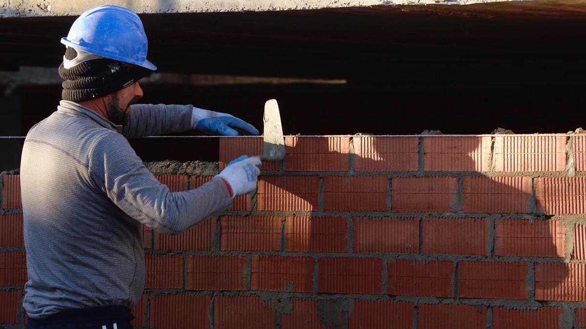 Un trabajador de la construcción levanta una pared de ladrillo.