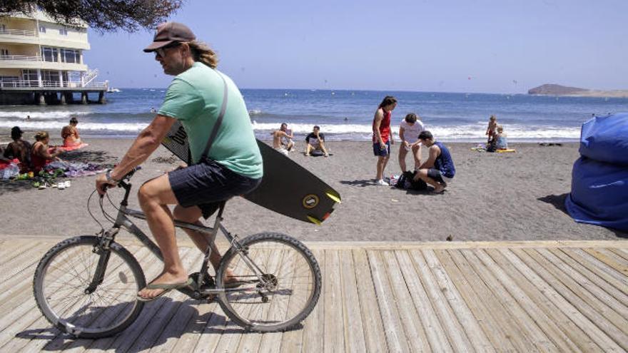 Un joven se mueve en bicicleta por el paseo marítimo de la playa de El Médano.