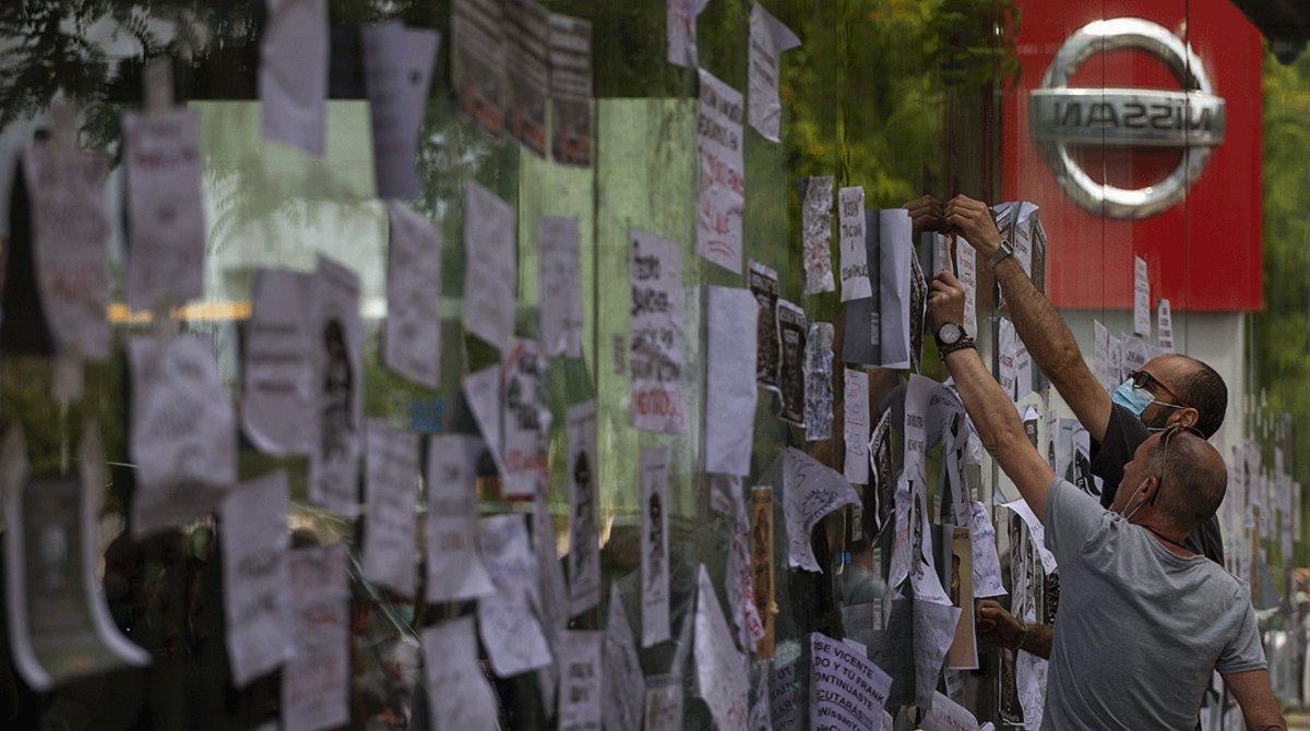 Trabajadores de Nissan pegan carteles contra el cierre de la planta de la Zona Franca en el escaparate de un concesionario de la marca en Barcelona, el viernes 29 de mayo.