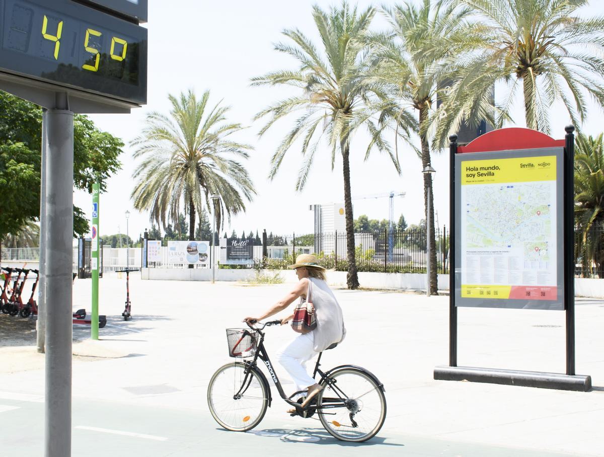  Una mujer en bicicleta pasa junto a un termómetro de calle en Sevilla que marca 45 grados.