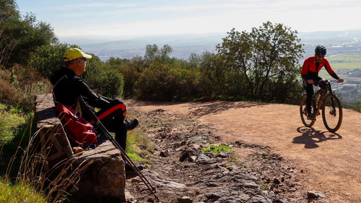 Un senderista descansa junto al sendero restaurado de la Cuesta del Reventón mientras observa pasar a un ciclista.