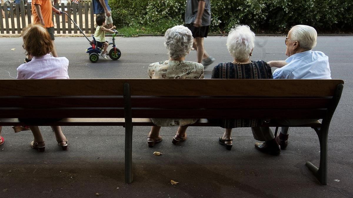 Un grupo de ancianos descansan en un banco en un parque de Barcelona