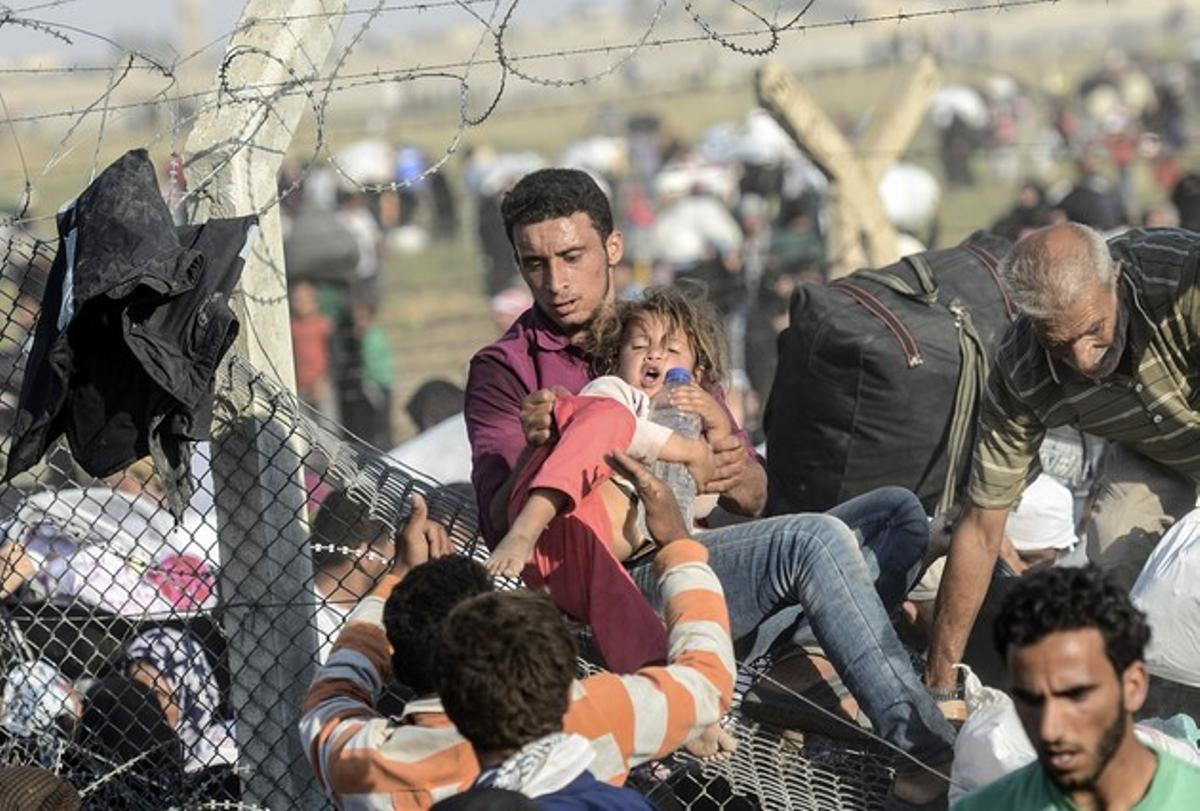 Un refugiado sirio hace pasar la frontera a un niño pequeño.