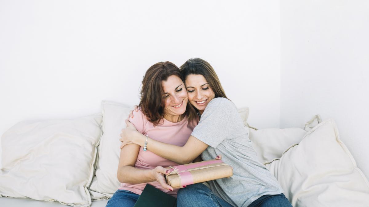 cheerful women with present hugging at home