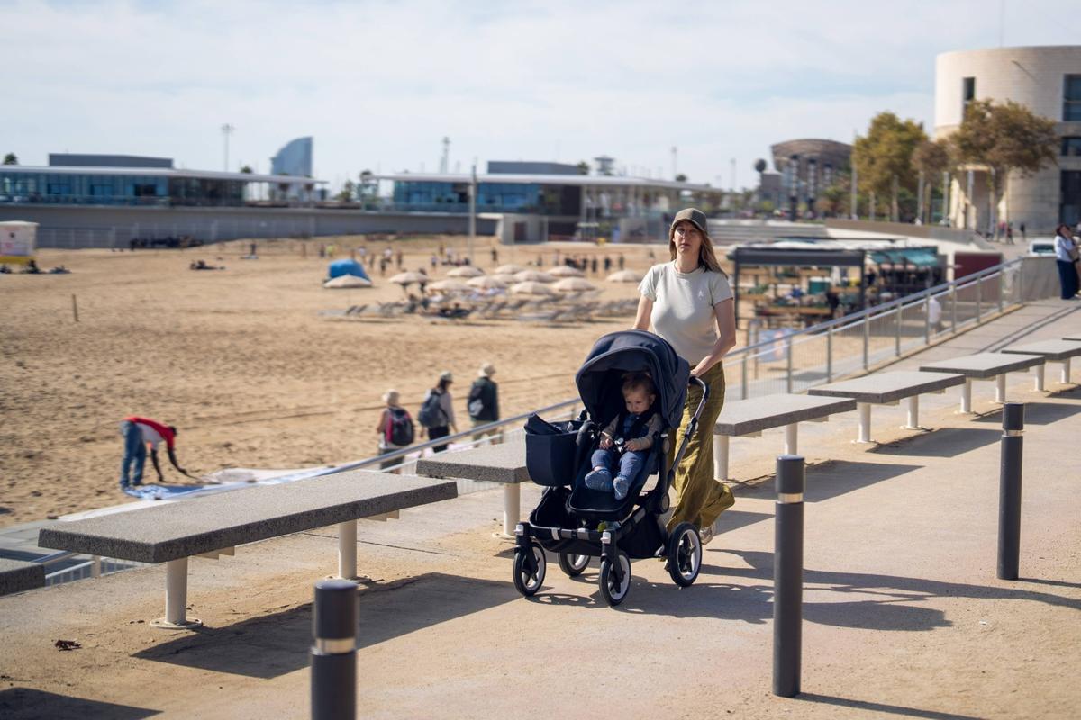 Una mujer pasea con su hijo delante de la playa de Barcelona.