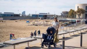 Una mujer pasea con su hijo delante de la playa de Barcelona.
