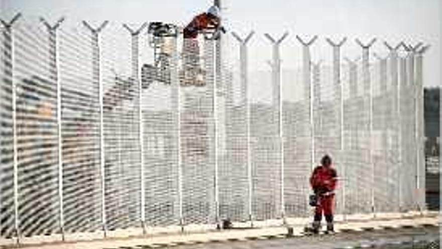 Dos operaris treballen en la construcció de la tanca.