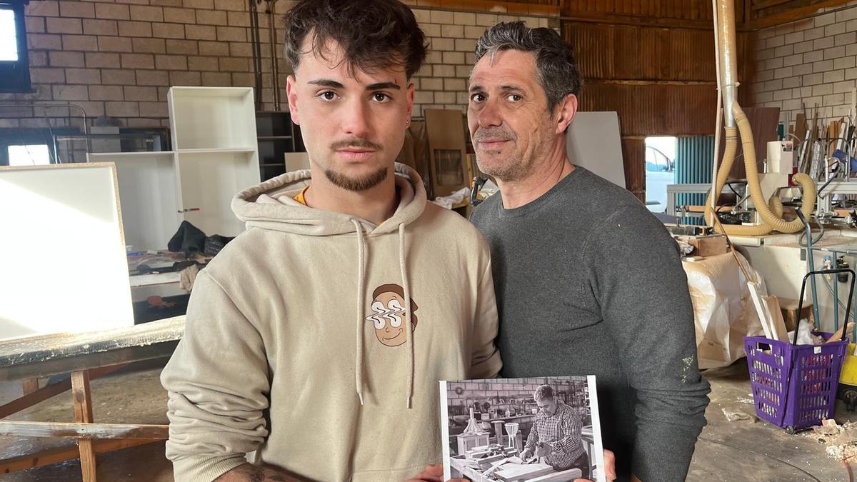 Su nieto, Nicolás, y su hijo, Francisco Nicolás, sostienen un cuadro de su abuelo en el taller de carpintería.