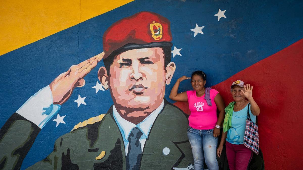 Dos mujeres posan para una fotografía junto a un mural de Hugo Chávez.