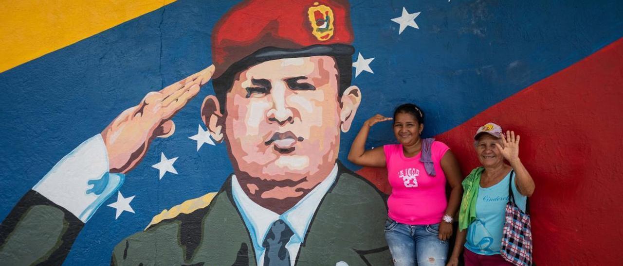 Dos mujeres posan para una fotografía junto a un mural de Hugo Chávez.