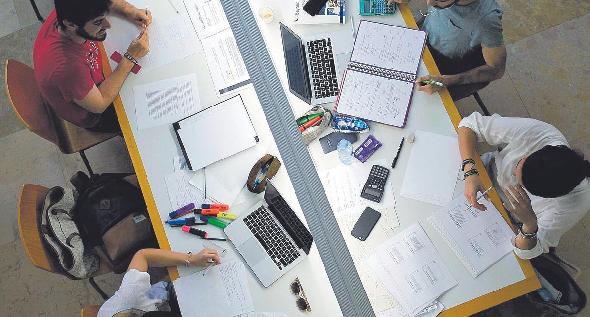 Universitarios preparando exámenes finales en la biblioteca, con sus resúmenes y ordenadores como apoyo.
