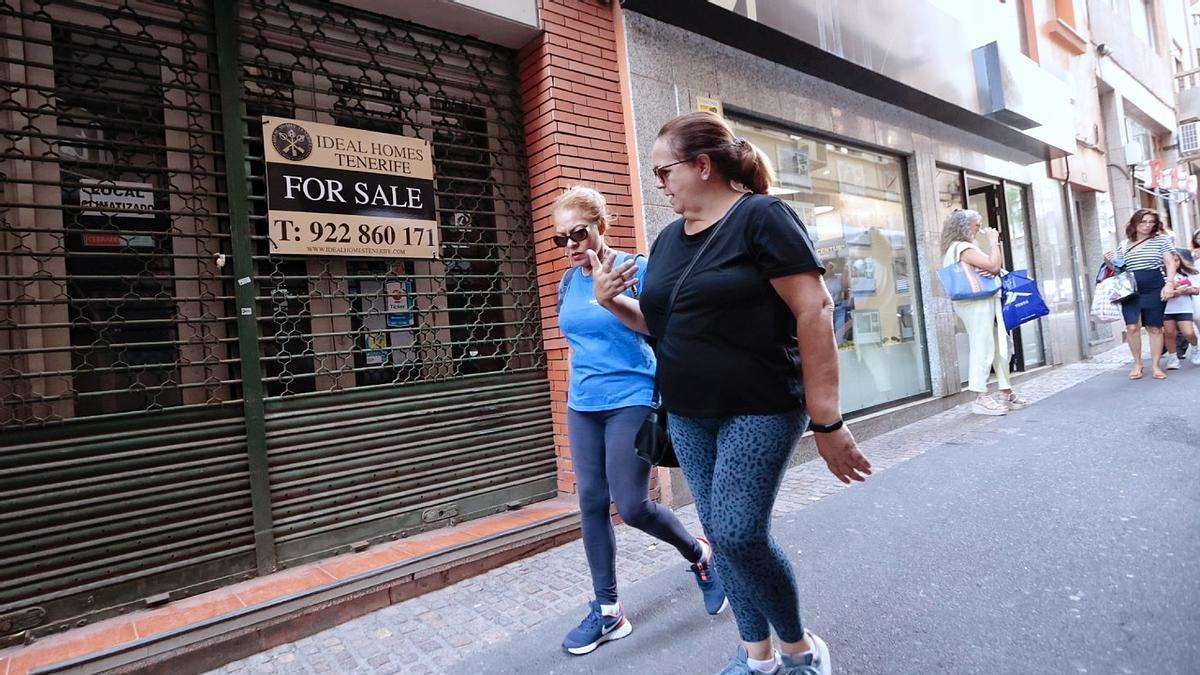 Dos personas pasan frente a un cartel de se vende. c