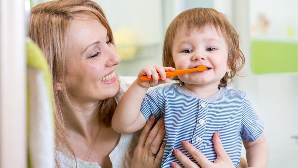 Un niño se lava los dientes de forma autónoma con la ayuda de su madre