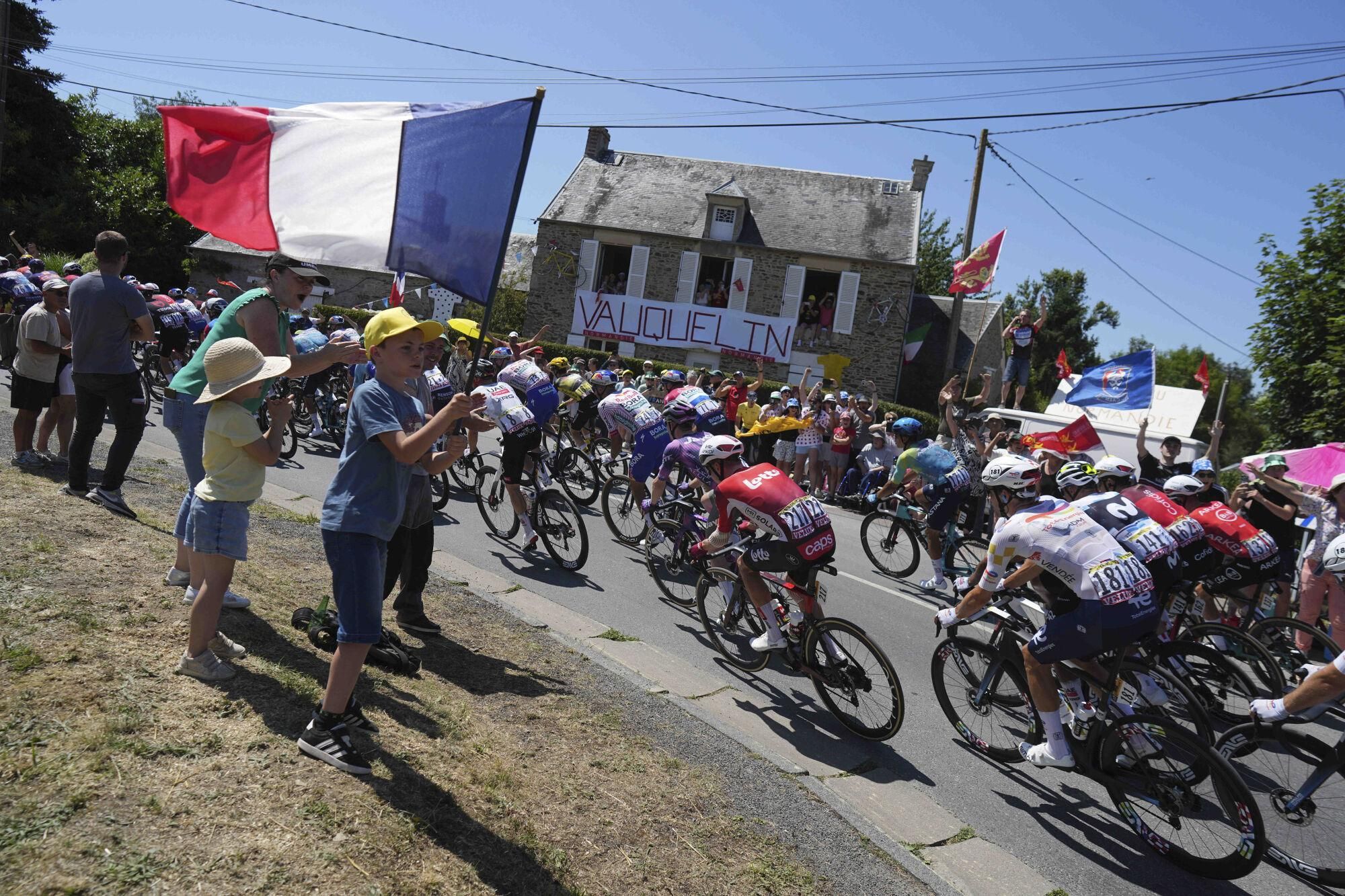 A boy waves a French flag as the pack rides during the sixth stage of the Tour de France cycling race over 201.5 kilometers (125.2 miles) with start in Bayeux and finish in Vire Normandy, France, Thursday, July 10, 2025. (AP Photo/Thibault Camus). EDITORIAL USE ONLY/ONLY ITALY AND SPAIN