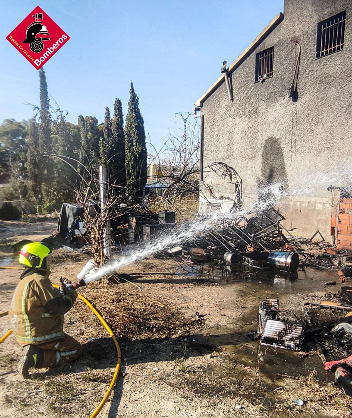 Un bombero enfría la fachada del chalet calcinado en Elche.