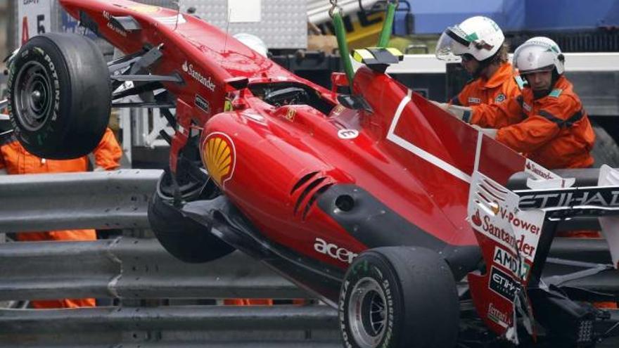 La grúa, con la ayuda de dos operarios, retira por encima de la valla el Ferrari de Alonso.