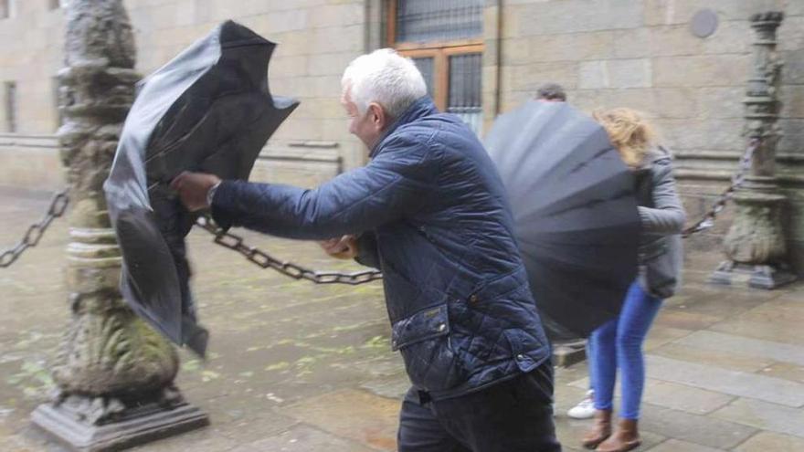 Turistas se protegen de la lluvia y el viento en Santiago, al salir del Hostal dos Reis Católicos. // X. Álvarez