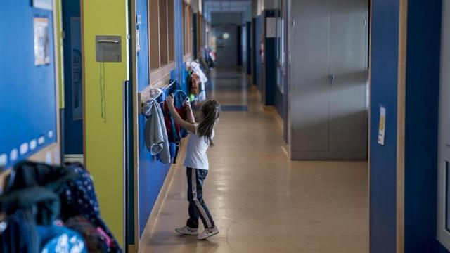Una niña cuelga su mochila en un perchero.