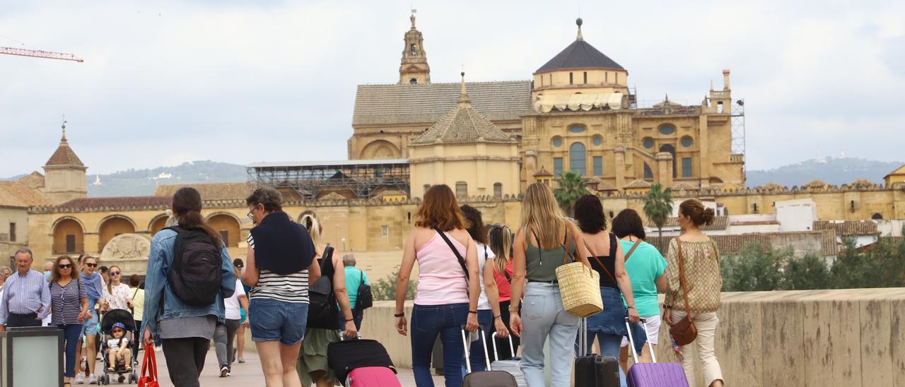 Turistas con maletas pasean por el Puente Romano de Córdoba, con la Mezquita-Catedral de fondo.