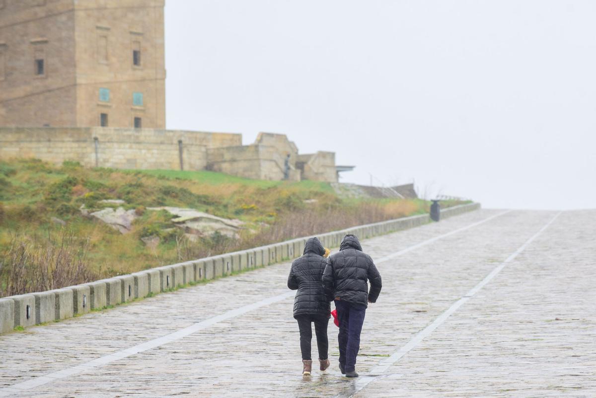 Dos personas pasean por la Torre de Hércules en un día de temporal