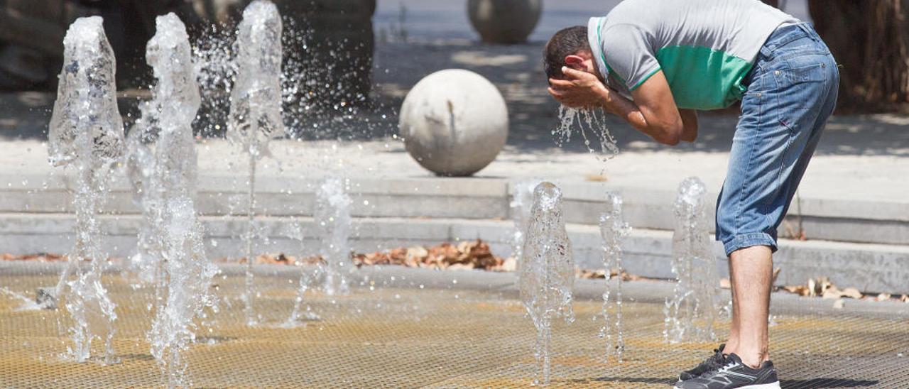 Un hombre se refresca en una fuente de Alicante.