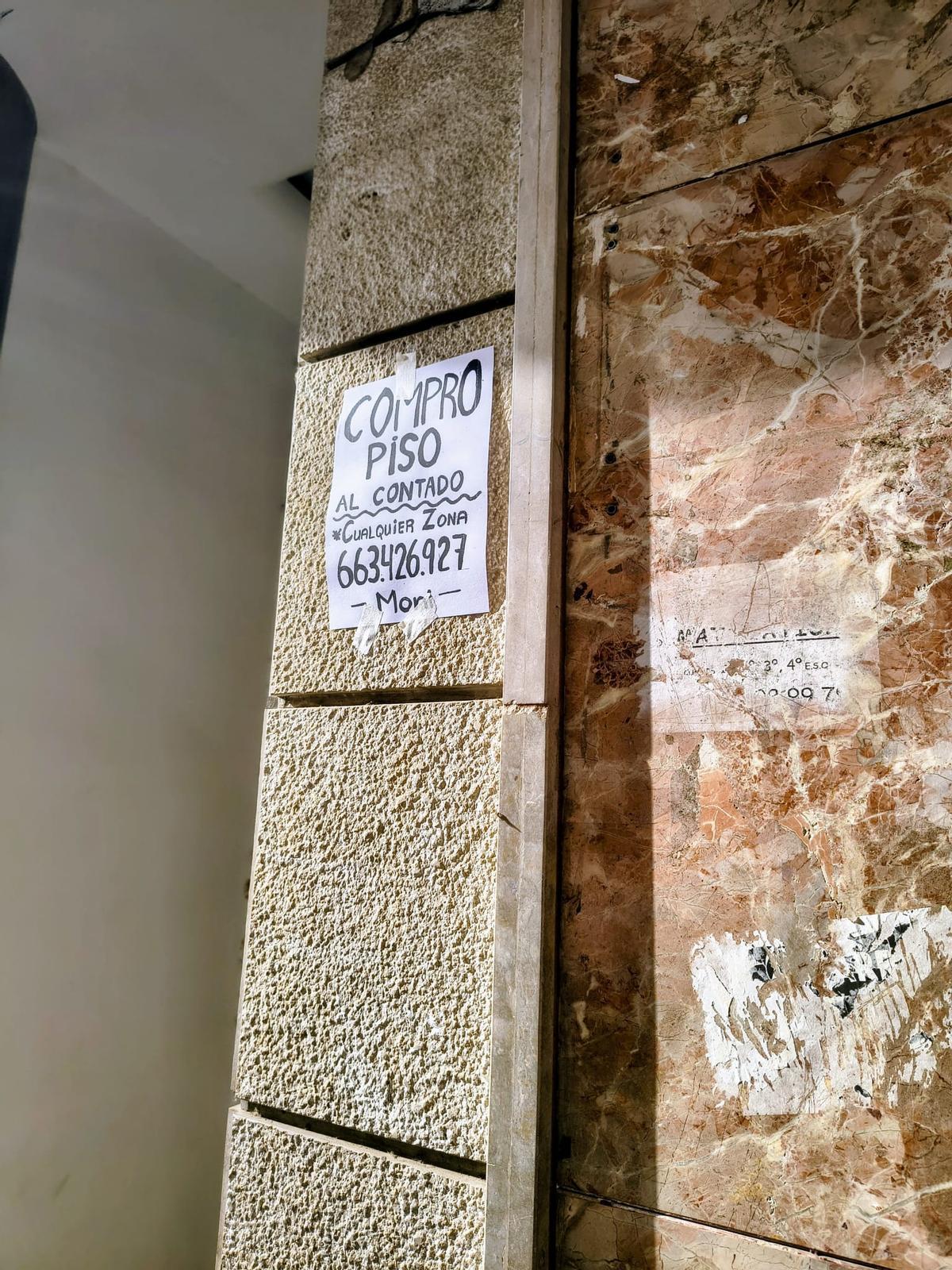 Cartel de "Compro piso" pegado de forma reciente en una fachada de la calle Cerdán de Tallada de Xàtiva.