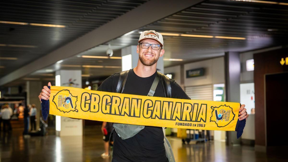 Luke Fischer posa con la bufanda del CB Gran Canaria en la terminal de llegadas del aeropuerto.