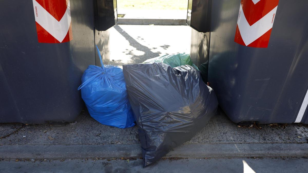 Bolsas de basura junto a unos contenedores en la calle.